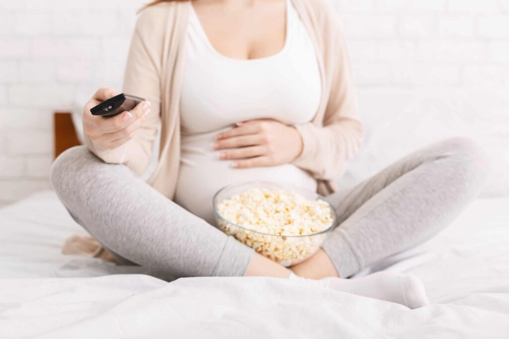 Pregnant woman watching TV and eating popcorn